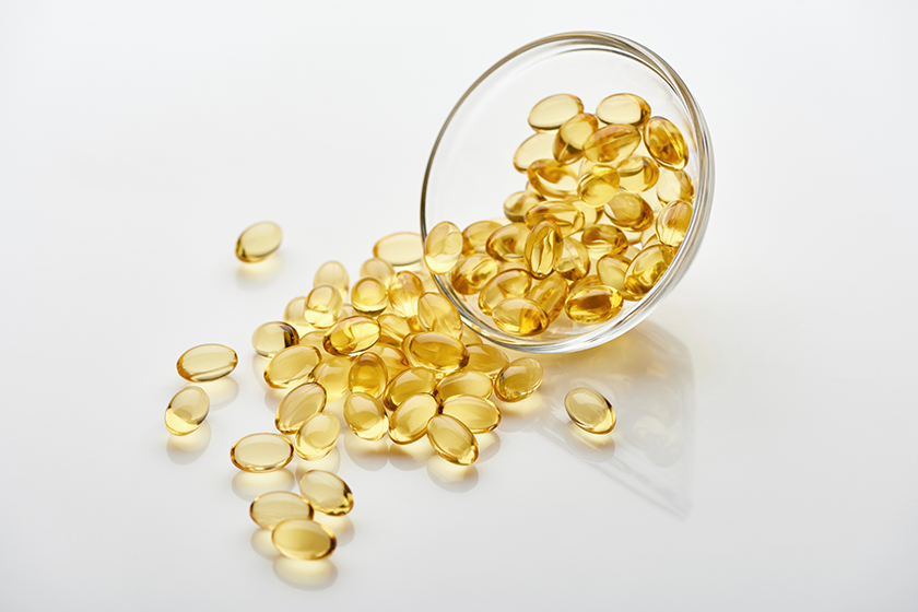 Golden fish oil capsules in glass bowl on white background